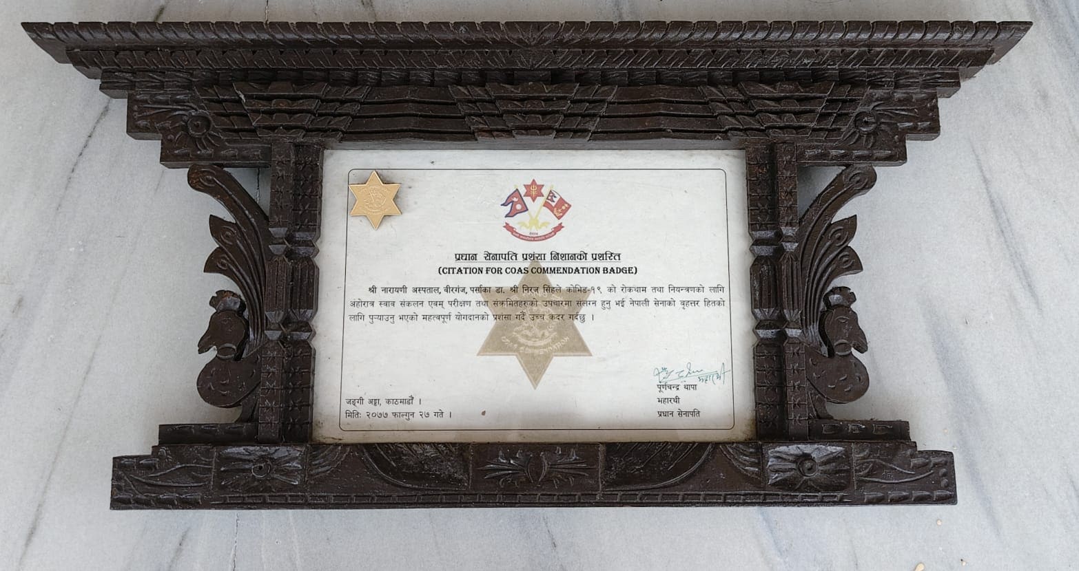 Citation for the Chief of Army Staff Commendation Badge naming Dr. Niraj Singh of Narayani Hospital, displayed in a carved wooden frame.